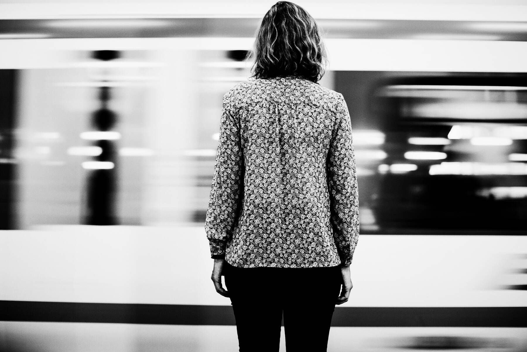 Mulher de costas numa plataforma, com o trem passando em movimento